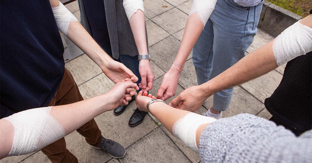 Six people show their bandaged forearm after donating blood together.