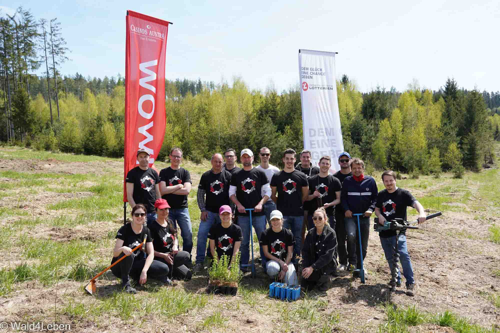 Group of 17 people at “Forest4Life” in front of two flags of Casinos Austria and Austrian Lotteries.