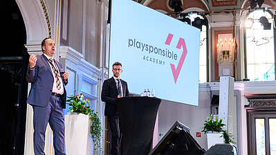 Zwei Männer mit Anzug und Krawatte referieren auf der Bühne des Casino Baden über die Bedeutung von Playsponsible