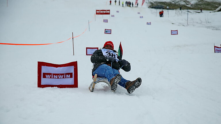 Mann rodelt im Schnee den Berg hinab.