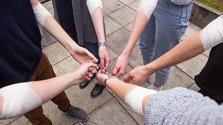 Six people show their bandaged forearm after donating blood together.