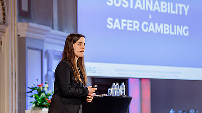 Dame mit langen Haaren in Hosenanzug lehnt sich auf der Bühne an ein Stehpult während sie Best Practice Beispiele zeigt.