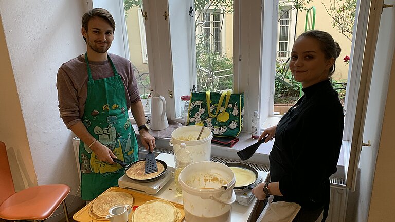 Junger Mann und junge Frau backen Palatschinken für Bedürftige.