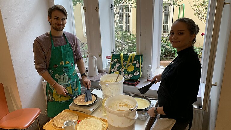 Junger Mann und junge Frau backen Palatschinken für Bedürftige.