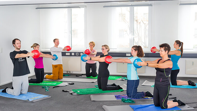  Menschen in Sport-Outfits bei Pilates-Übungen mit Ball auf Turnmatten