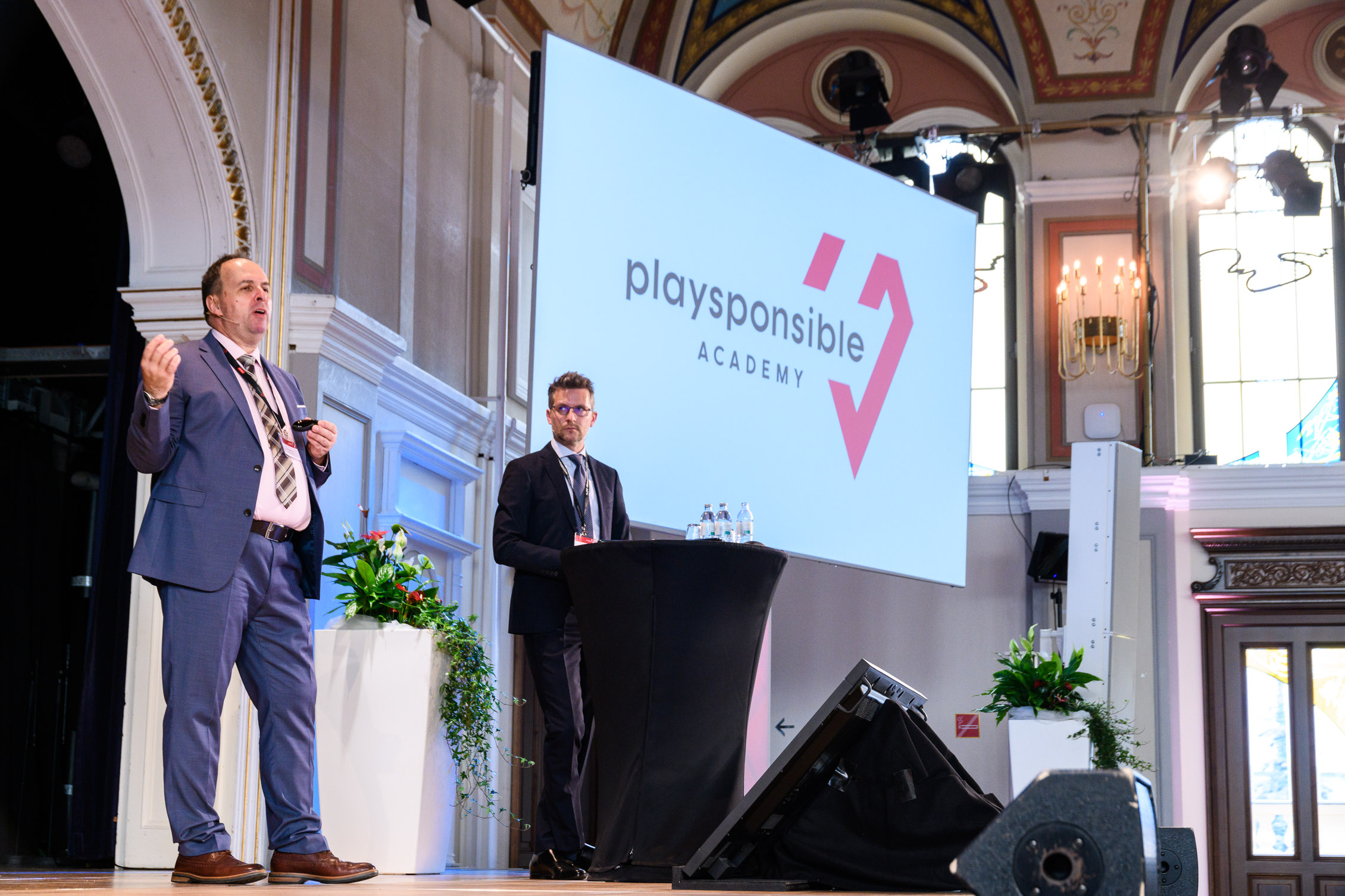 Two men in suits and ties present a talk about the importance of Playsponsible on the stage of Casino Baden.